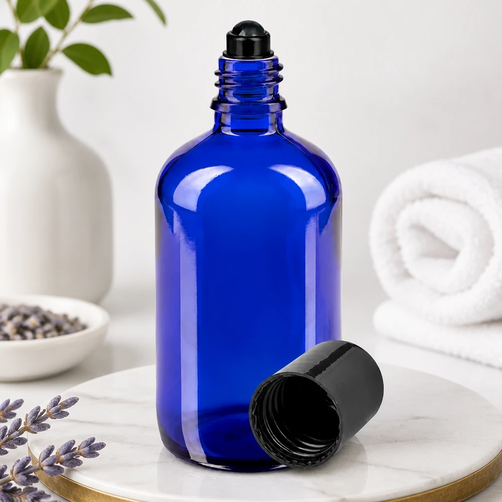 Blå 100 ml glasflaske med sort rullekugle og afmonteret låg på marmor