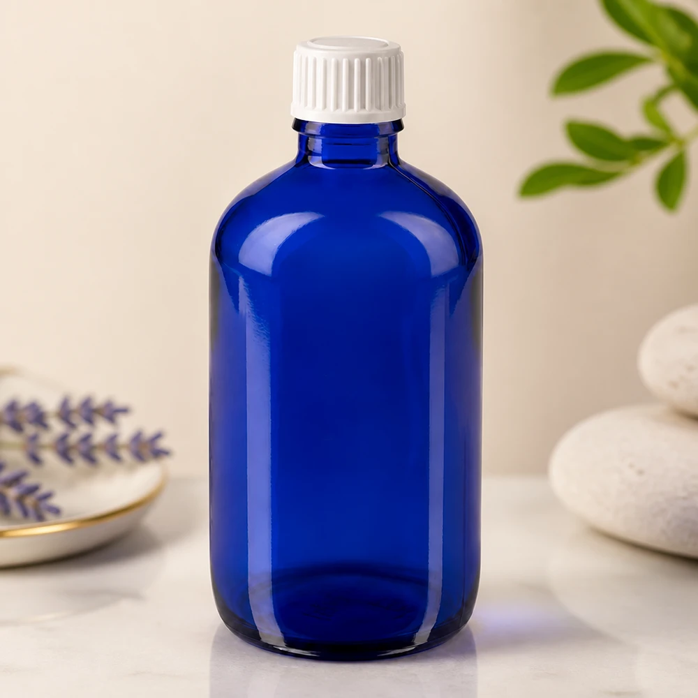 Apoteksflaske blå 100ml skruelåg hvid stk. Blå 100 ml glasflaske med hvid børnesikret låg på en marmoroverflade ved siden af lavendel