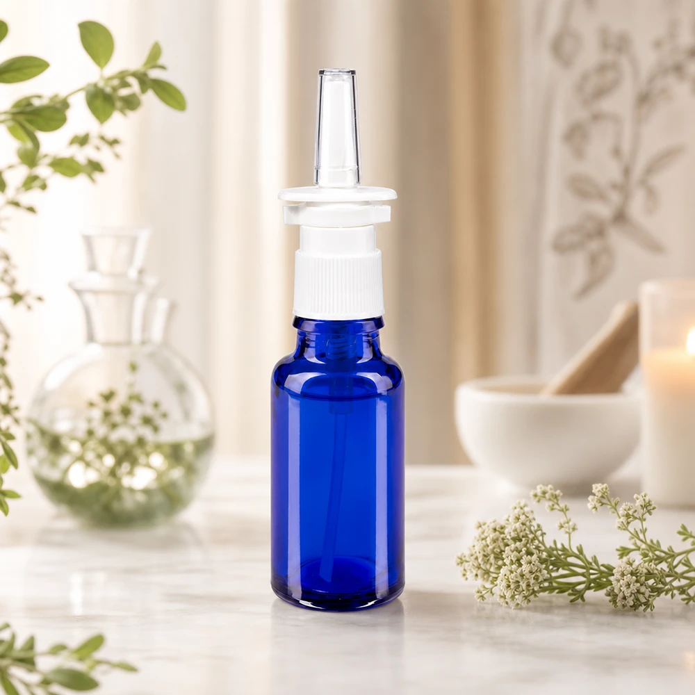 Blåt 20 ml apoteksglas med hvid næsespray-pumpe og gennemsigtig applikatordyse foran en naturlig baggrund