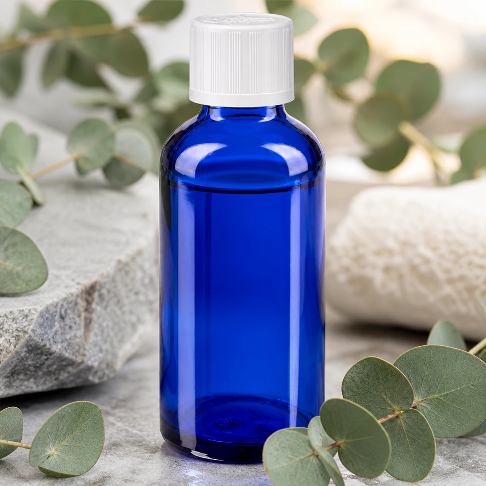 Koboltblå 50 ml apotekerflaske med hvid KiSi-prop på en natursten mellem eukalyptusgrene