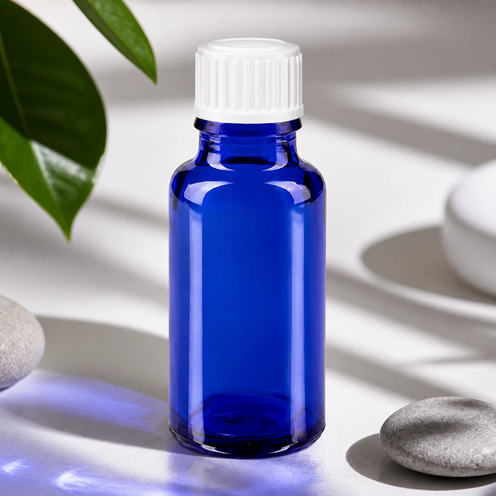 Apoteksflaske blå 20 ml skruelåg hvid pc Blå 20 ml glasflaske med hvid prop ved siden af natursten og grønne blade