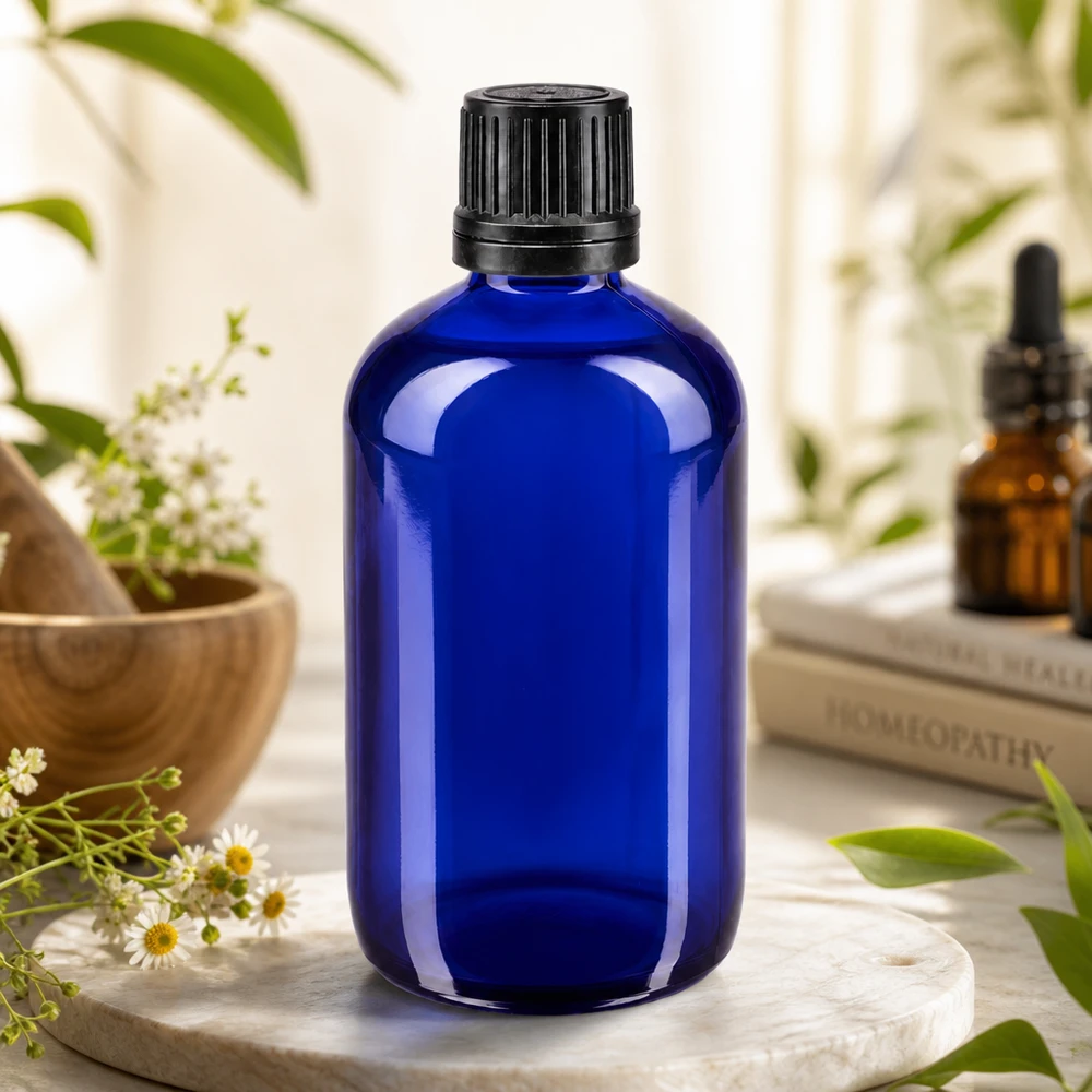 Blå 100 ml apotekerflaske med riflet sort låg mellem kamilleblomster og lægeurter