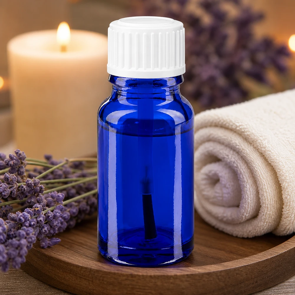 Aromaterapiflaske på 10 ml i blåt apotekerglas med hvid penseldyser ved siden af lavendelblomster