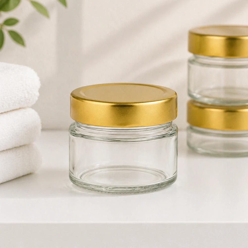 80 ml rund krukke med BasicSeal-låg guld dyb UNiTWIST 80 ml rund krukke med BasicSeal-låg guldfarvet dyb i en badeværelsesatmosfære med hvide håndklæder til kosmetik