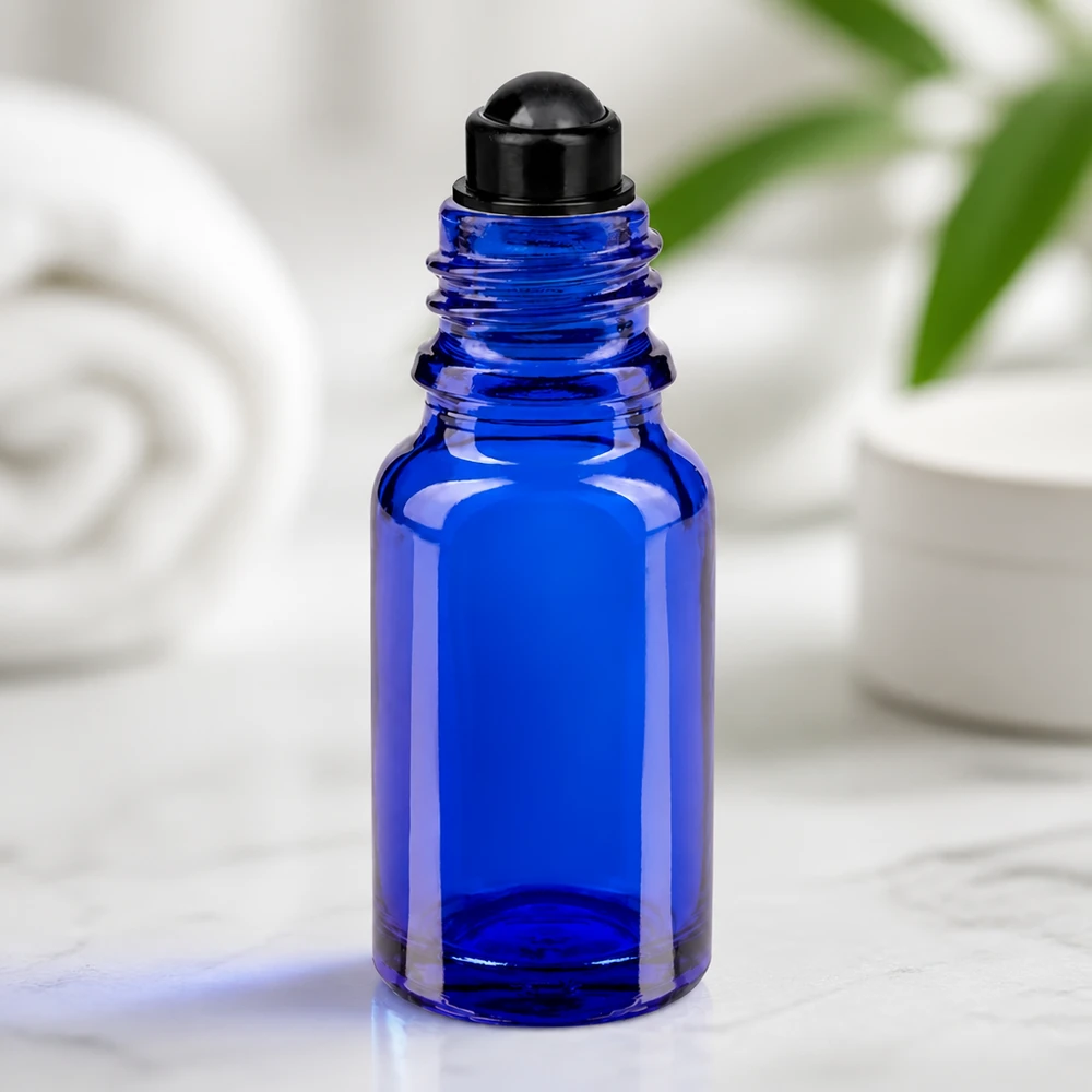 Apoteksflaske blå 10 ml roll-on-hætte sort Blå 10 ml glasflaske med sort roll-on-hoved på marmor foran en hvid baggrund