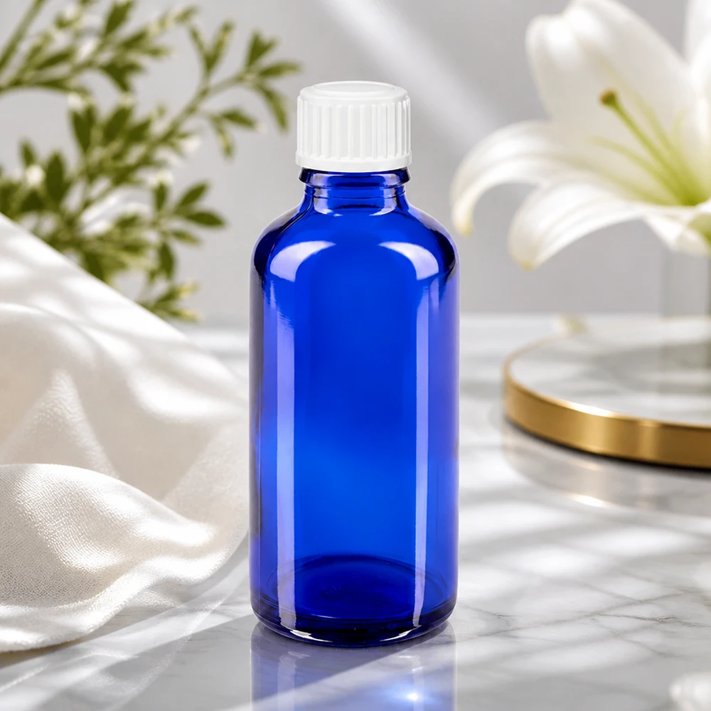Apoteksflaske blå 50ml skruelåg hvid stk. Blå 50 ml glasflaske med hvid skruelåg ved siden af en hvid lilje på en marmoroverflade