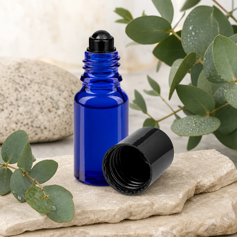 Blå 10 ml ApoGlas-roll-on-flaske med sort låg ved siden af eukalyptusgrene på natursten