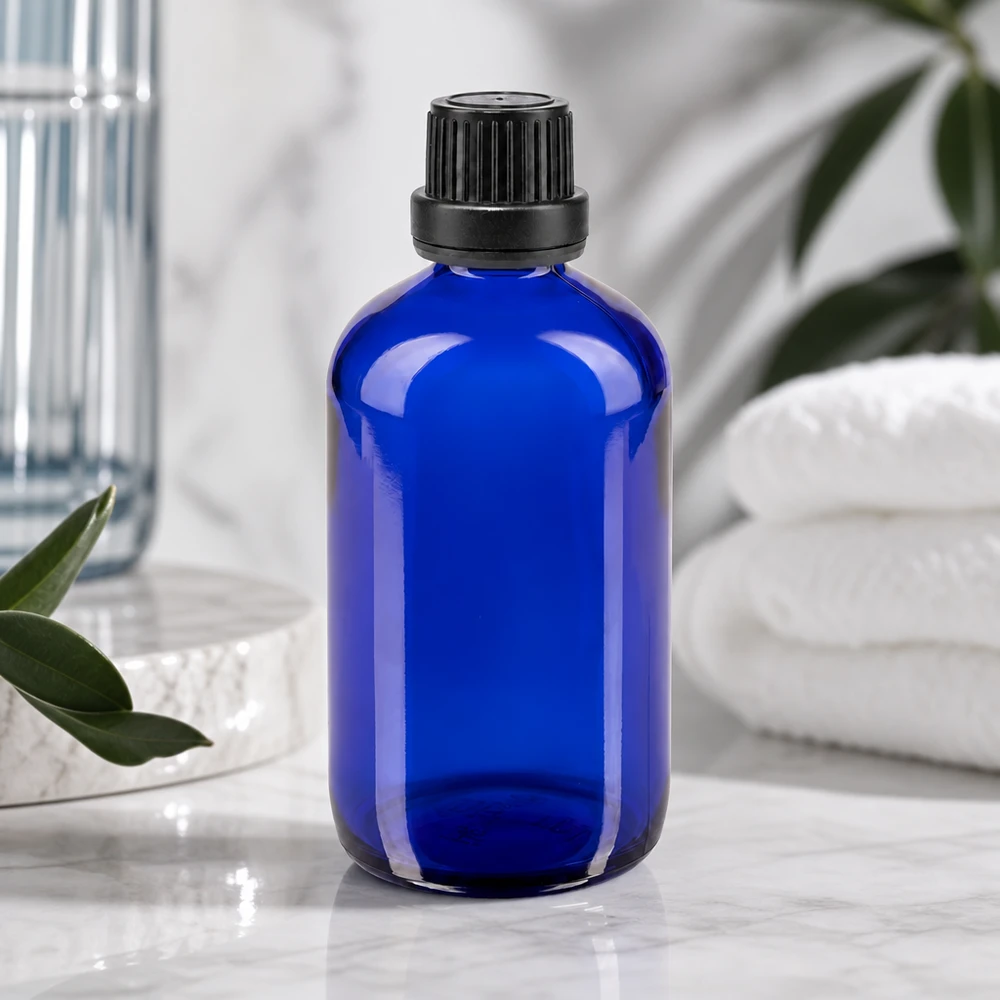 Apoteksflaske blå 100 ml skruelåg sort tæt OV Blå glasflaske på 100 ml med ribbet sort låg ved siden af hvide håndklæder og grønne planter
