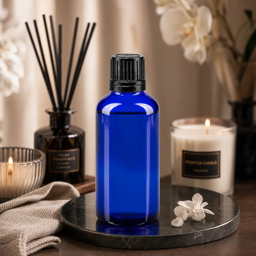 50 ml blå glasflaske med sort skruelåg på et marmorfad med stearinlys og duftlampe
