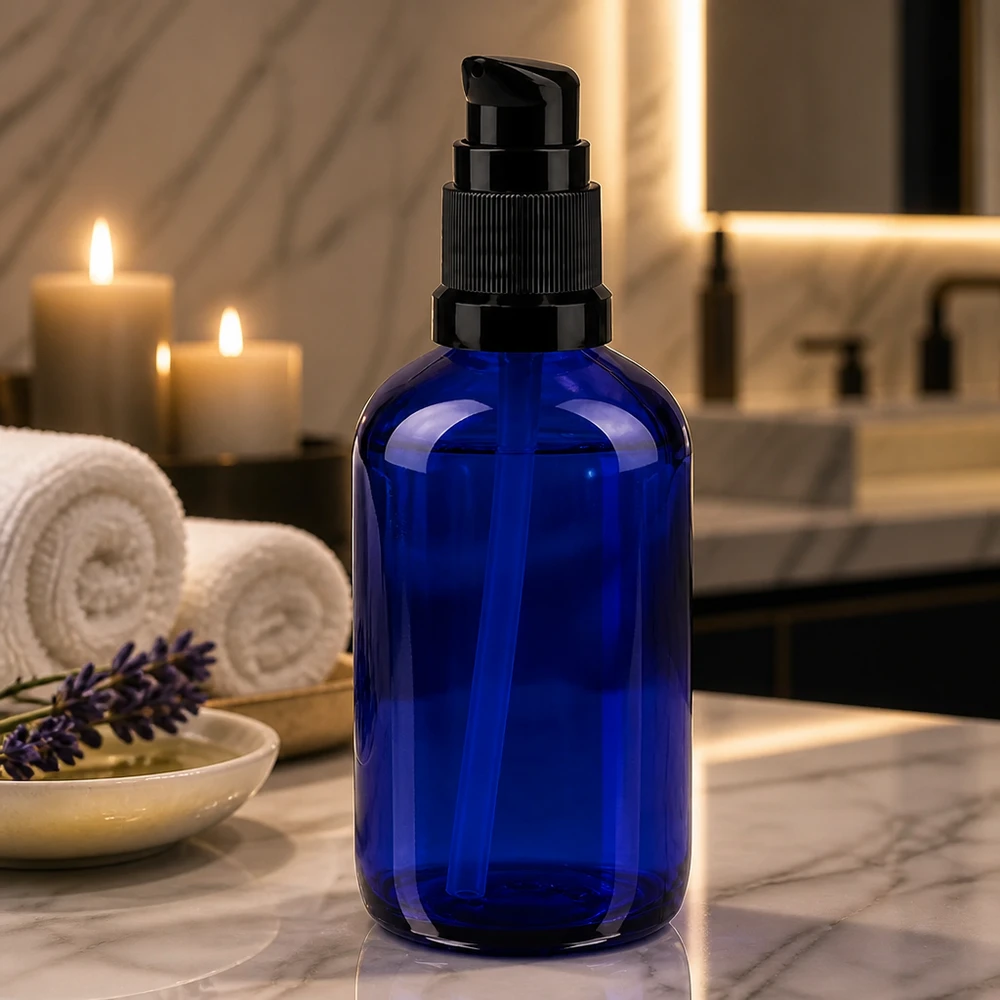 Elegant 100 ml pumpeflaske af blåt apotekerglas med sort dispenser på marmor ved siden af stearinlys
