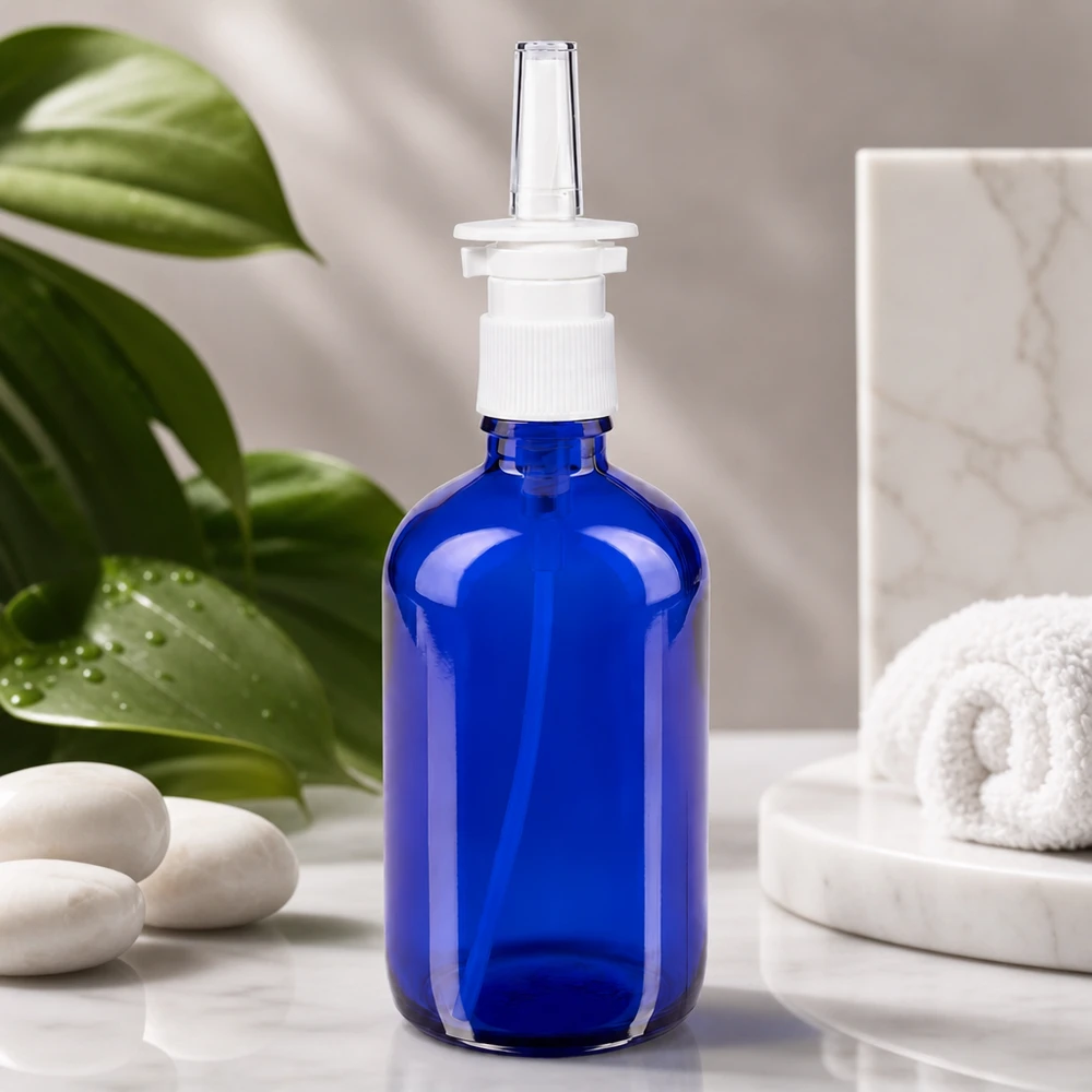 Koboltblå 100 ml glasflaske med næsesprayhoved på hvid marmor ved siden af wellness-sten