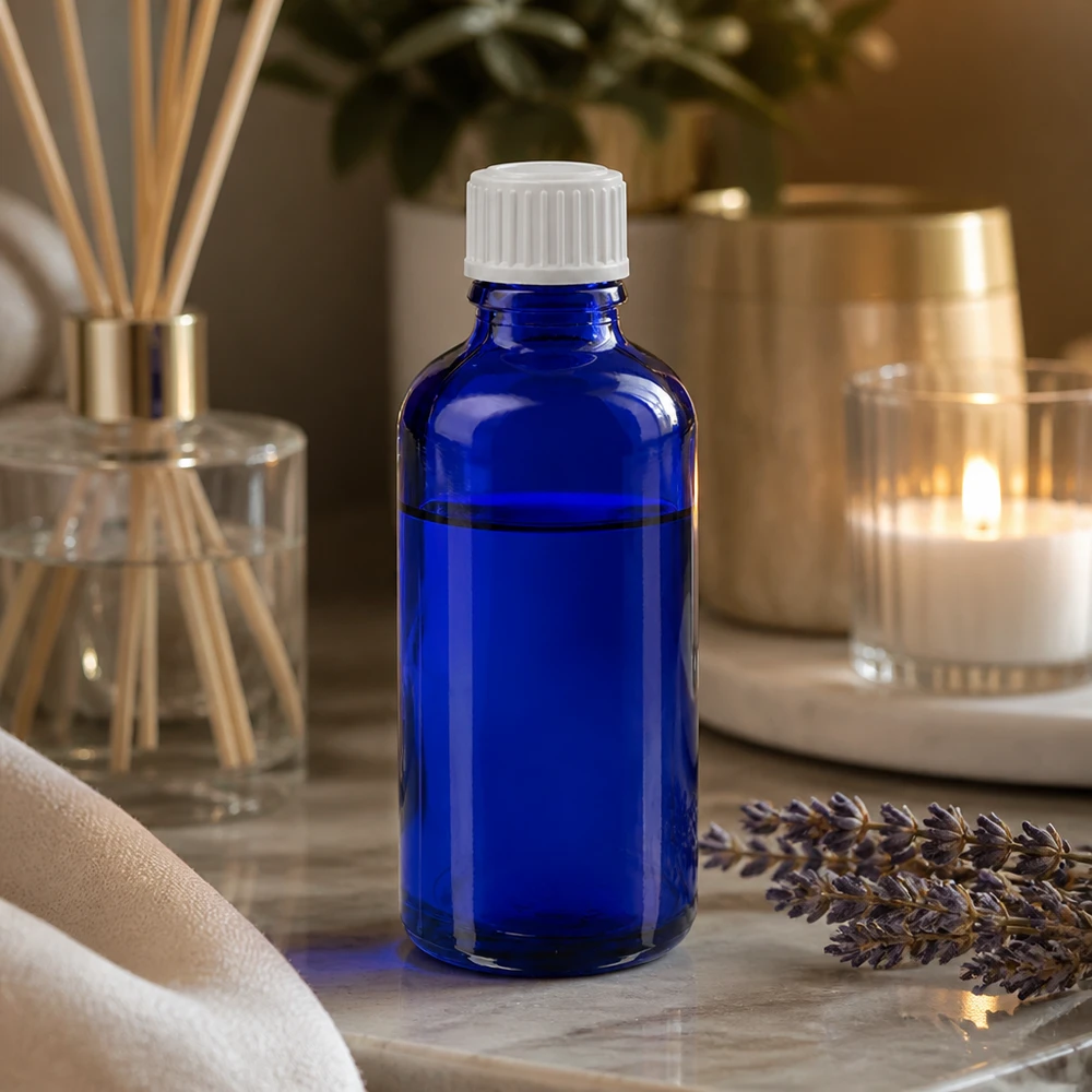 Apoteksflaske blå 50ml dråbetæller hvid 0,8mm stk. 50 ml blå glasflaske med dråbeforsegling på marmor ved siden af lavendel og en duftdiffusor