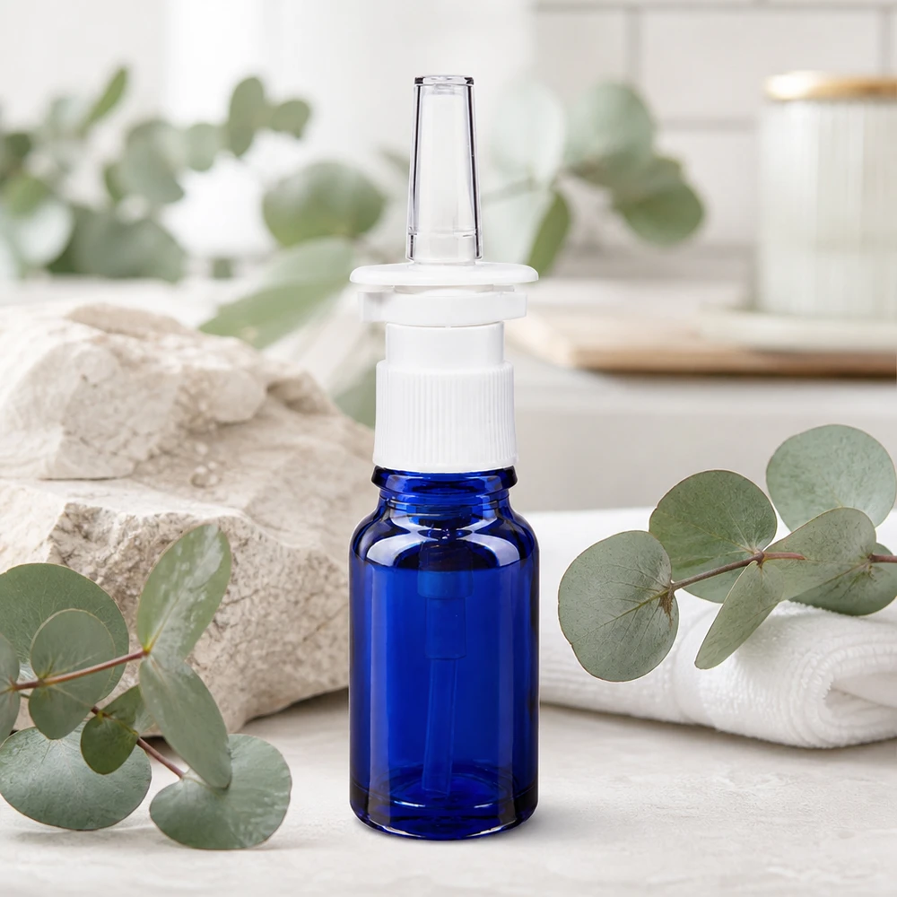 Blå 10 ml glasflaske med gennemsigtig næsespray-dyse foran en naturlig eukalyptusbaggrund