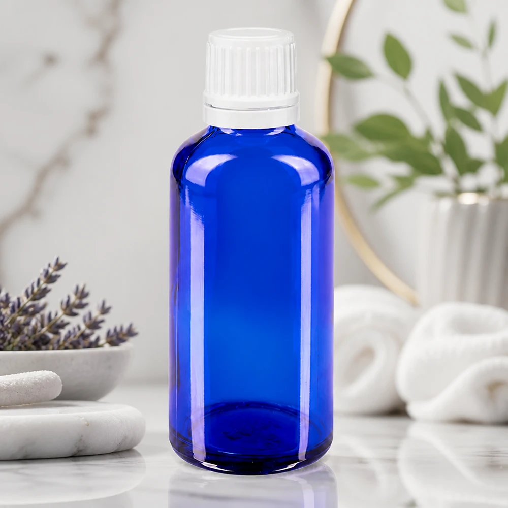 Apoteksflaske blå 50ml dryp v. 1,2 mm hvid OV Blå glasflaske på 50 ml med hvid skruelåg på marmor ved siden af lavendel