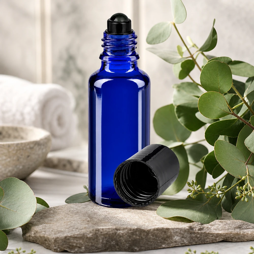 Koboltblå 30 ml glasflaske med sort roll-on-hoved på en natursten mellem eukalyptusgrene