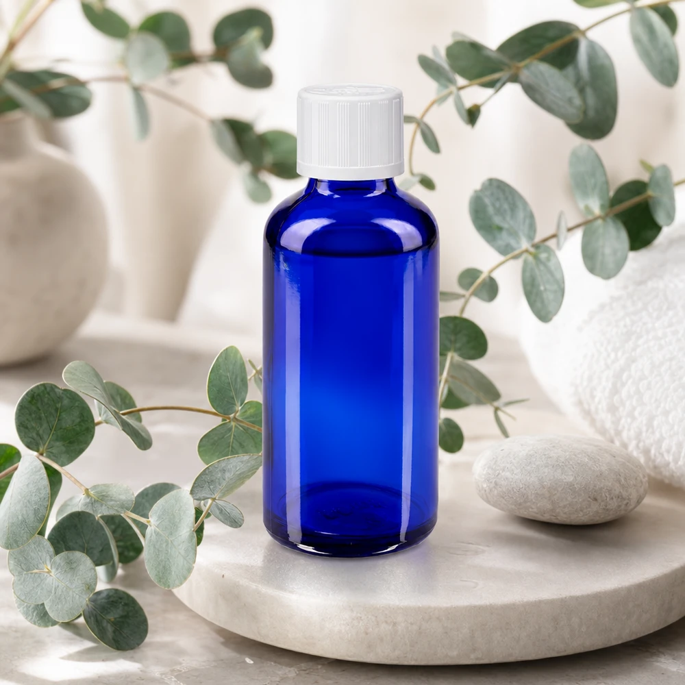 Apoteksflaske blå 50 ml skruelåg hvid KiSi St 50 ml apotekerflaske, blå med hvid sikkerhedslåg, på marmorunderlag med eukalyptus