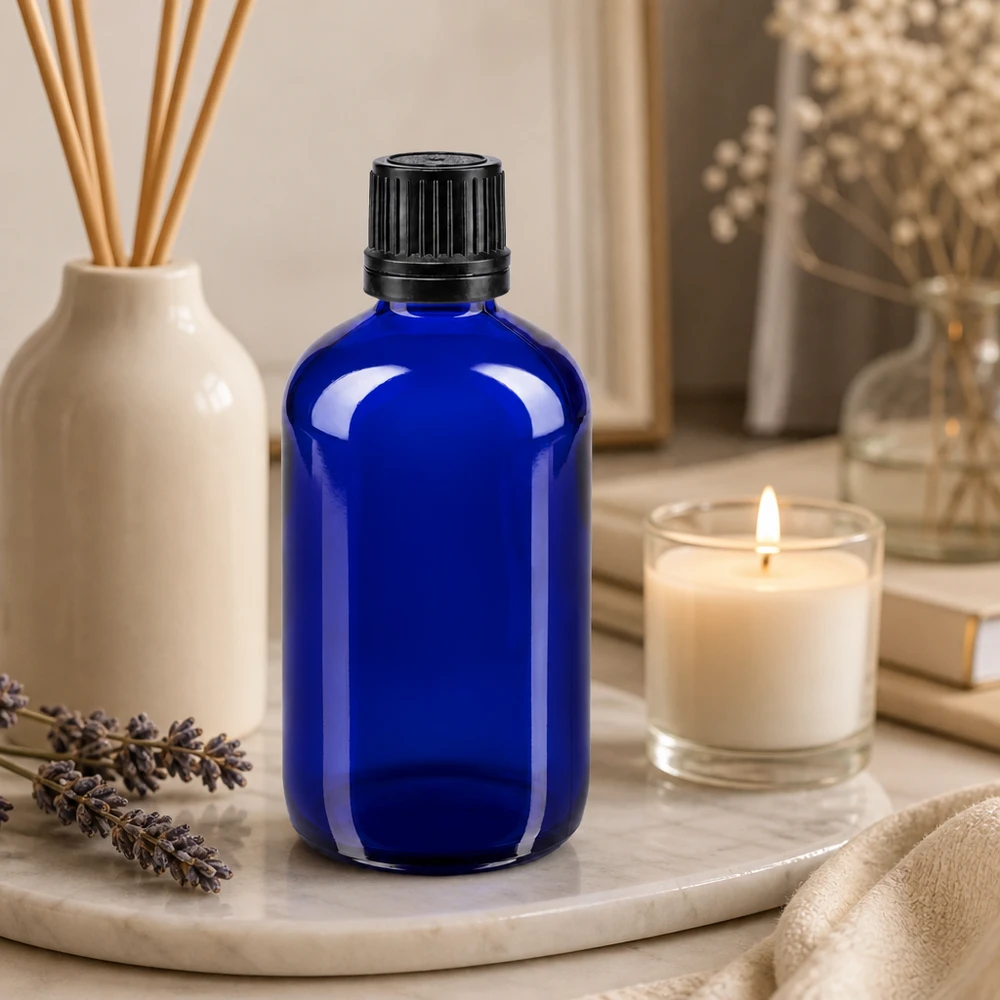 Apoteksflaske blå 100 ml skruelåg sort hældeprop r. OV 100 ml blå glasflaske med sort dråbepropp på et marmorfad med lavendel og et stearinlys