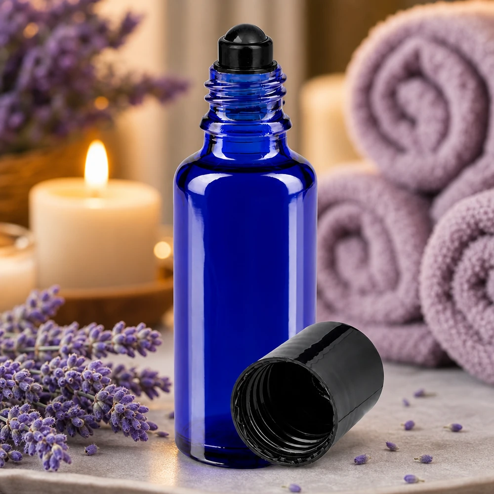 Apoteksflaske blå 30 ml roll-on-hætte sort En koboltblå 30 ml rulleflaske af apotekerglas med sort hætte ved siden af lavendelblomster og stearinlys