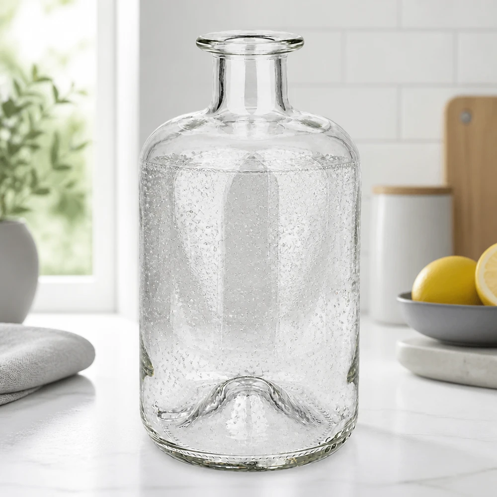500 ml apoteksflaske »500ml Glasflasche "Luna" ohne Verschluss UNiTWIST« uden lukning UNiTWIST® Apotekerflaske Luna 500 ml med bobletekstur på en hvid køkkenbordplade ved siden af citroner og planter