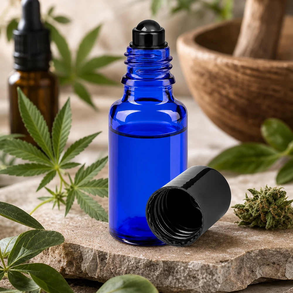Apoteksflaske blå 20 ml roll-on-hætte sort Lille 20 ml roll-on-flaske af blåt apotekerglas ved siden af en cannabisplante og en morter