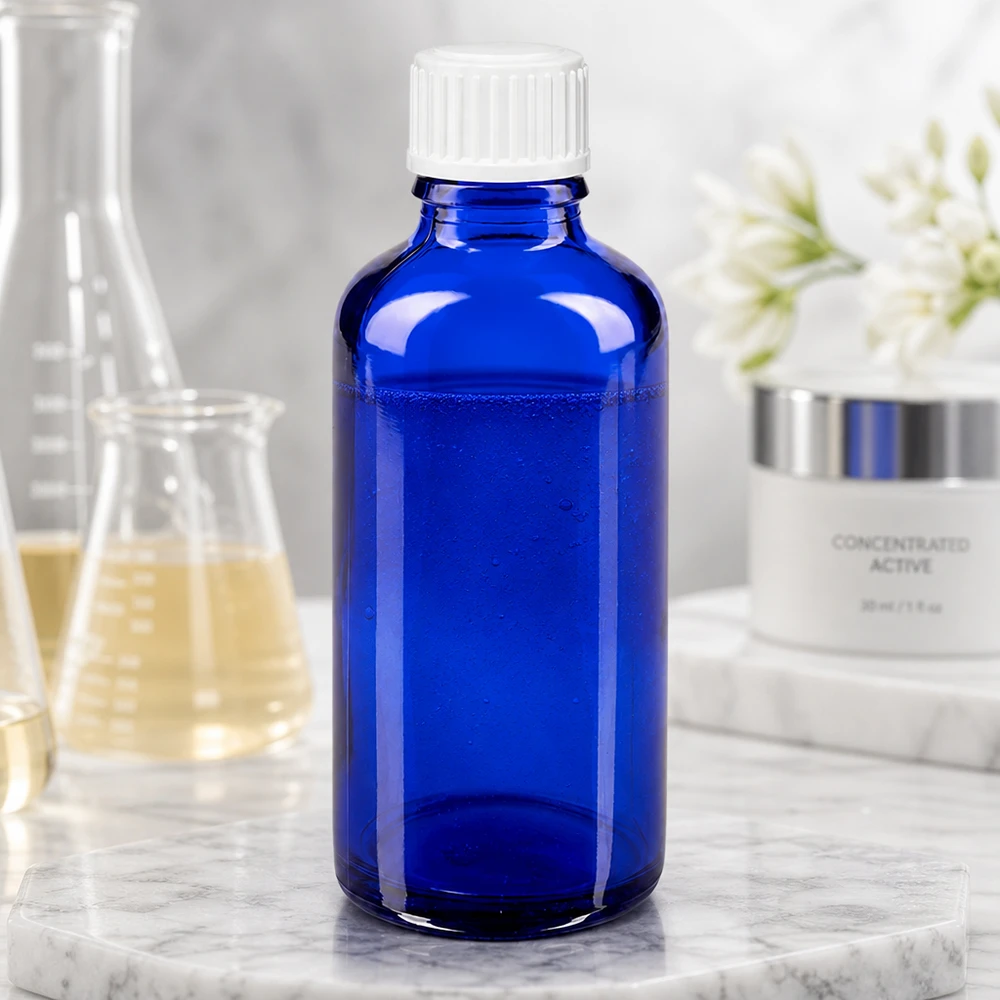 Apoteksflaske blå 50ml skruelåg hvid stk. Koboltblå 50 ml glasflaske med hvid skruelåg ved siden af en laboratoriekolbe og en hudplejecreme
