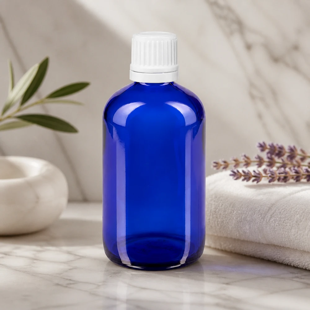 Blå 100 ml dråbeflaske af apotekerglas med hvid OV-prop på marmor