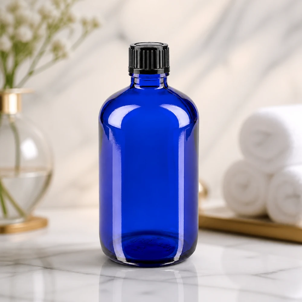 Cylindrisk blå glasflaske på 100 ml med riflet sort skruelåg på marmoreffekt