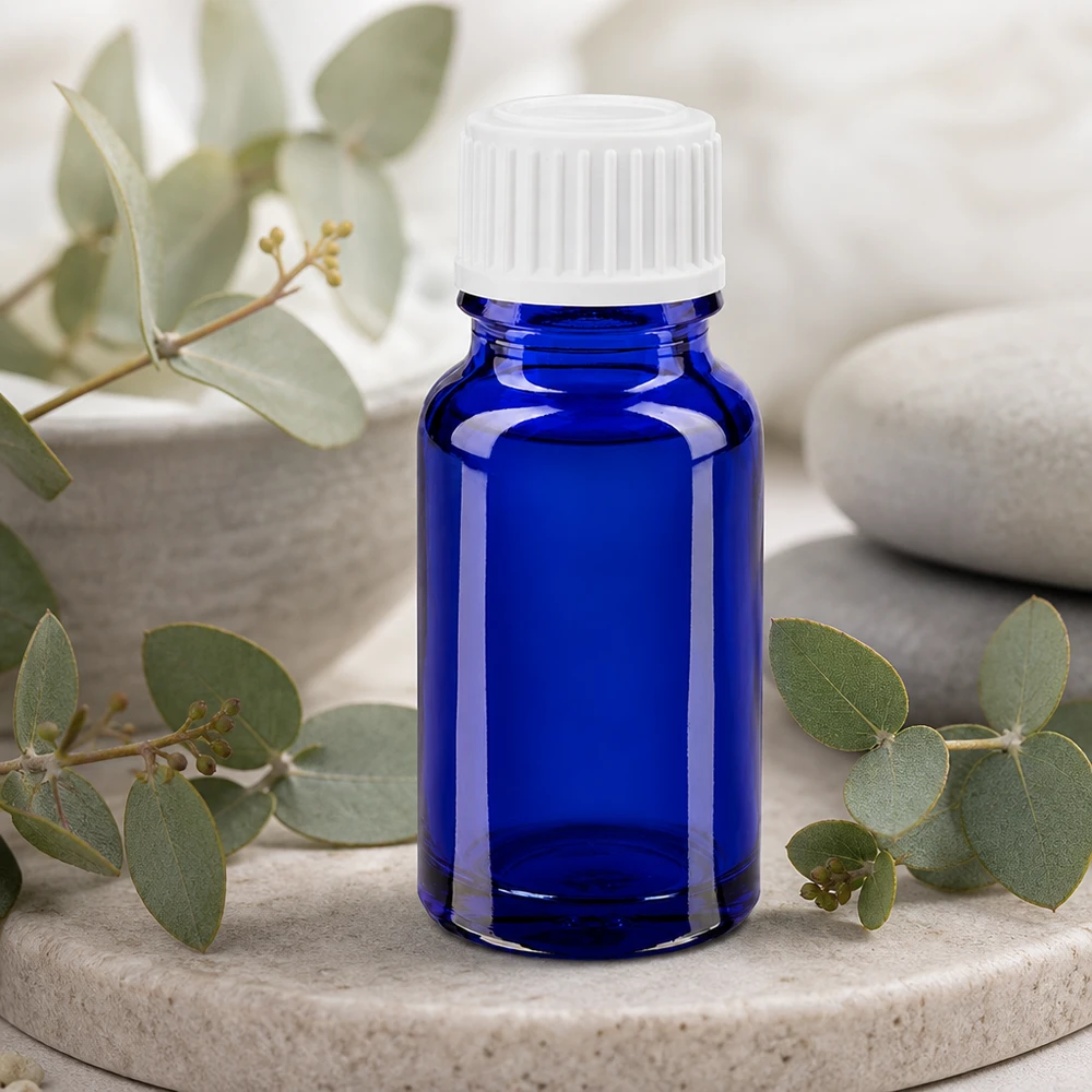 Koboltblå 10 ml glasflaske med hvid standardprop mellem eukalyptusgrene