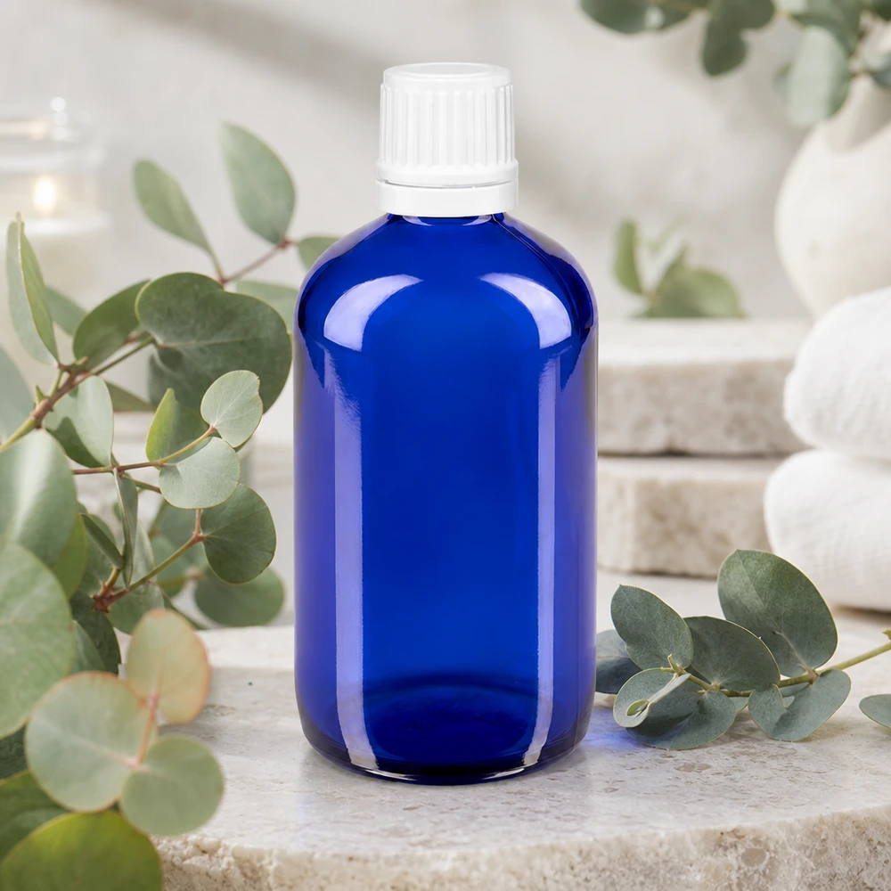 Koboltblå apotekerflaske på 100 ml med hvid sikkerhedslås på natursten med eukalyptusgrene