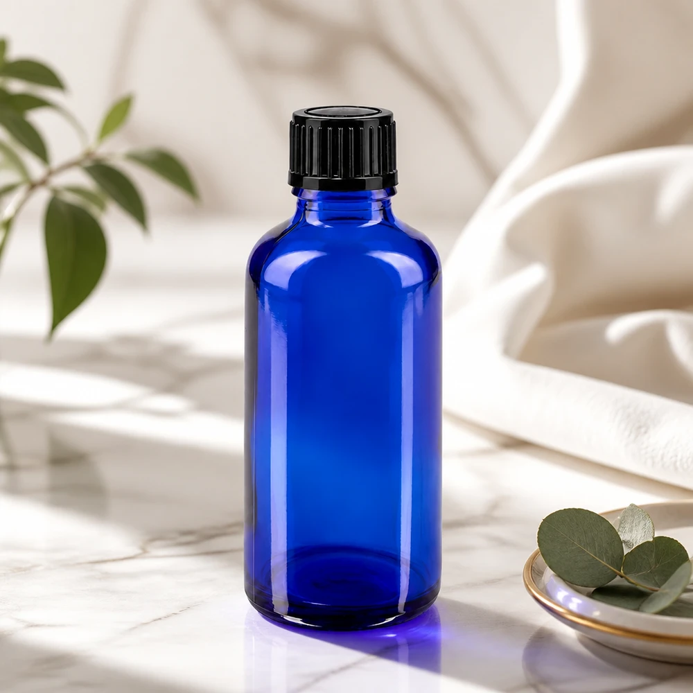 Apoteksflaske blå 50ml skruelåg sort pc Blå glasflaske på 50 ml med sort låg på marmor ved siden af eukalyptusblade