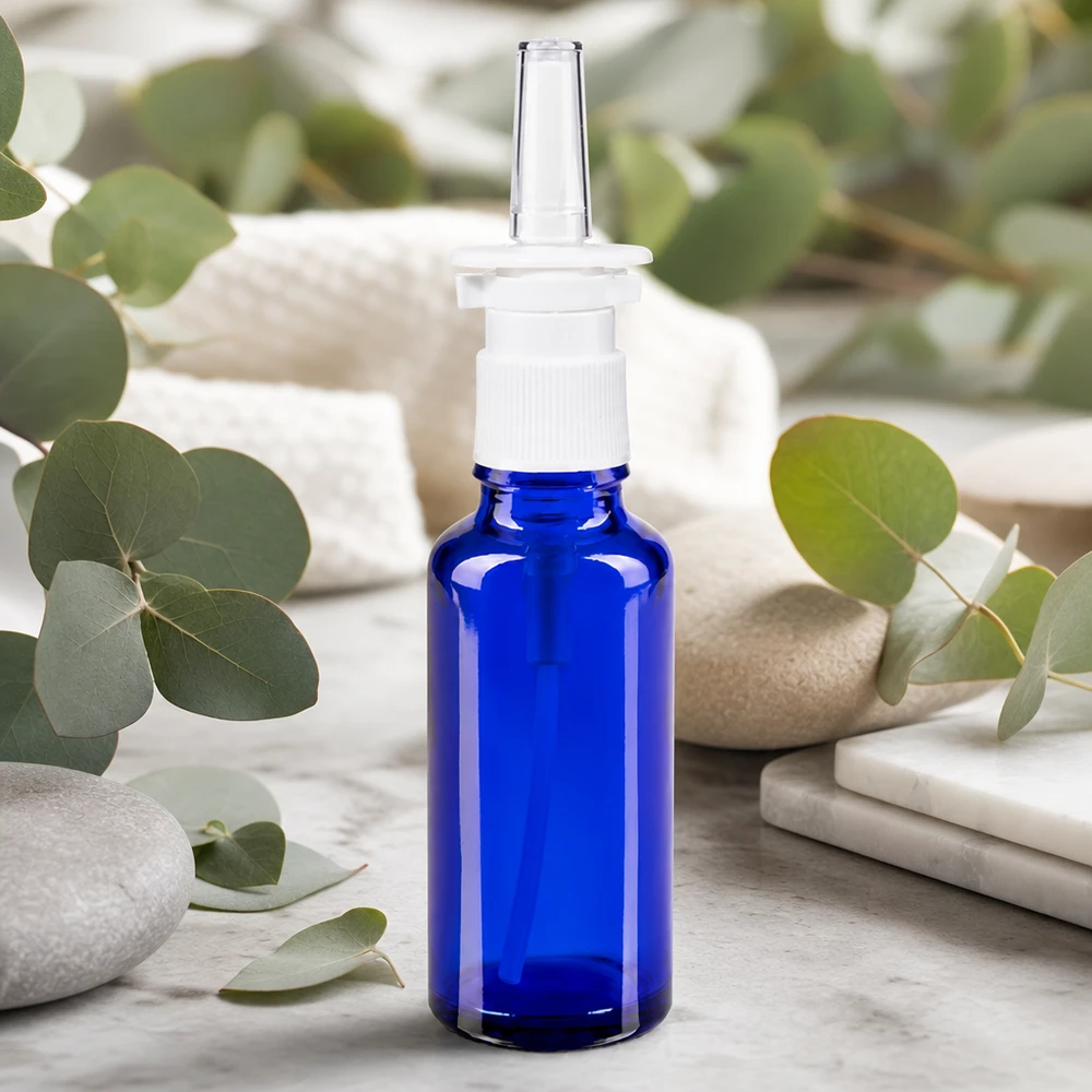 Apoteksflaske blå 30 ml næseforstøver hvid St 30 ml næsesprayflaske i koboltblå med hvidt pumpehoved og eukalyptusgrene som naturlig dekoration