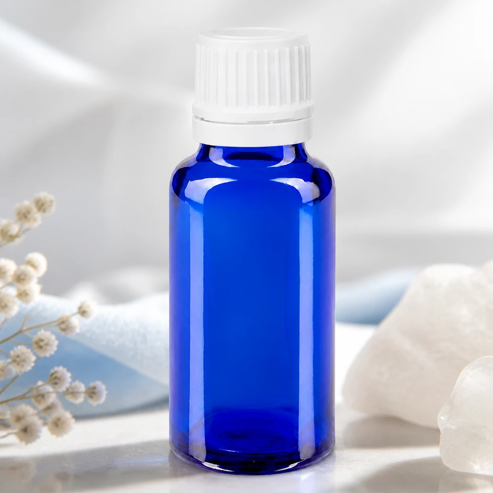 Koboltblå 20 ml apotekerflaske med hvid originalitetslukning ved siden af bjergkrystal og tørrede blomster