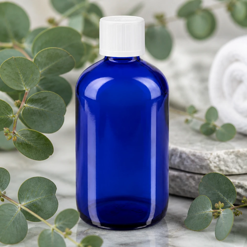 Apoteksflaske blå 100 ml dråbetæller hvid KiSi St Blå 100 ml dråbeflaske af apotekerglas med hvid KiSi-prop mellem eukalyptusgrene