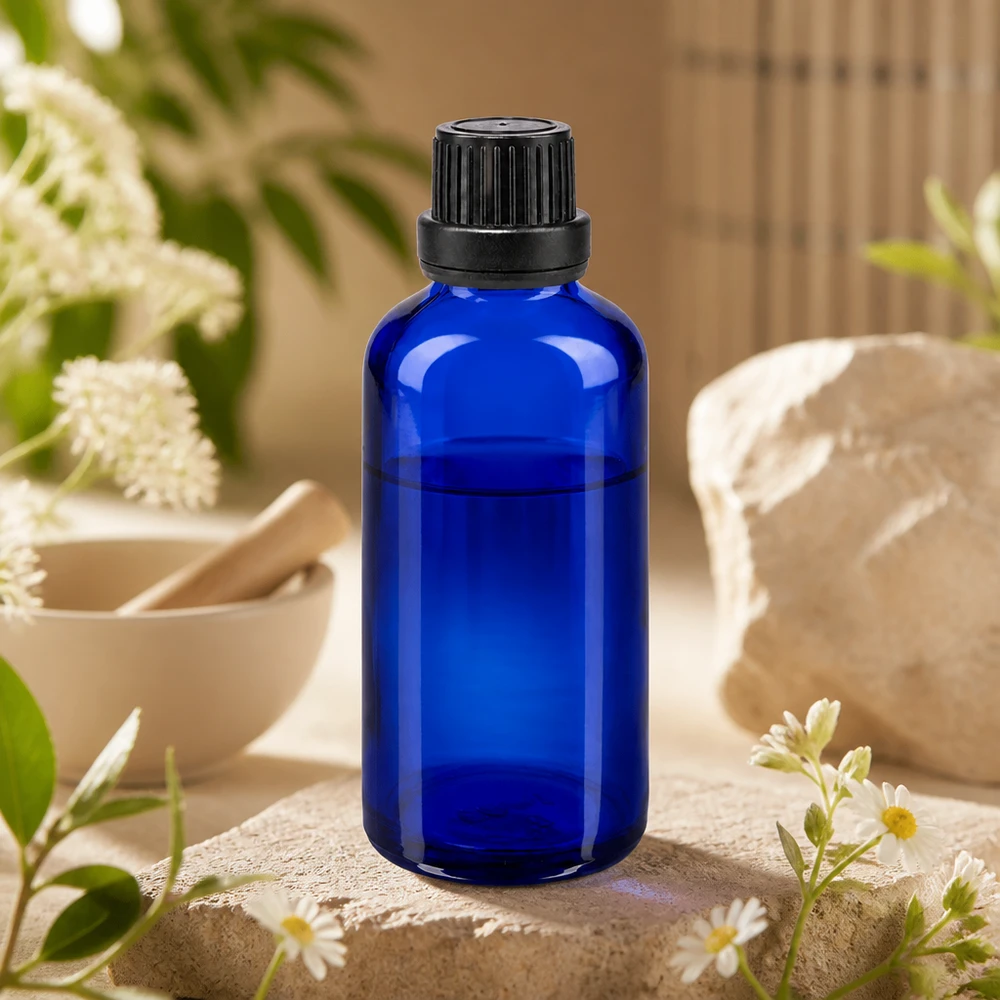 Apoteksflaske blå 50ml dryp v. Pr. 2mm sort OV Koboltblå 50 ml glasflaske med sort skruelåg på en natursten med kamilleblomster og en morter