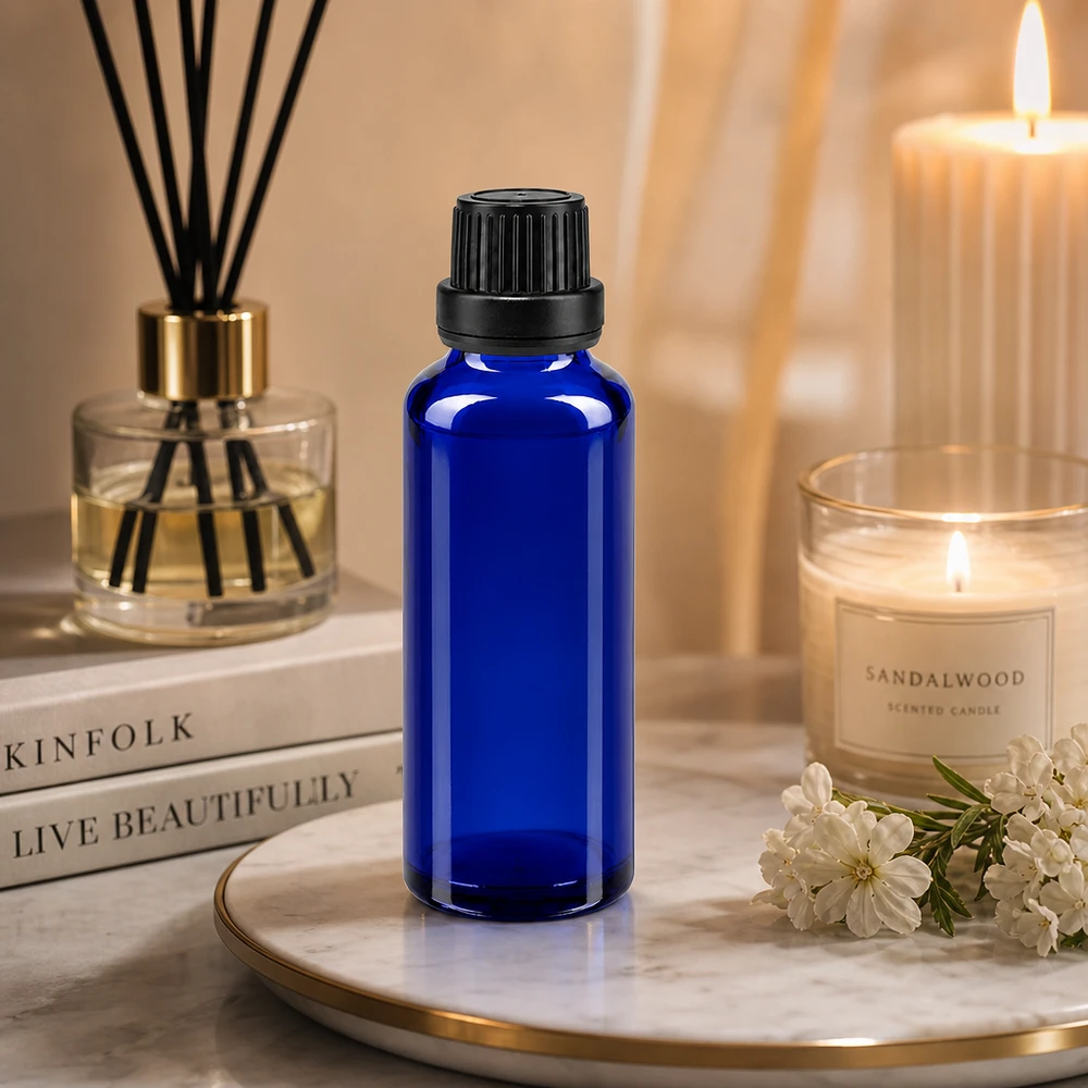 Apoteksflaske blå 30ml dryp v. Pr. 2mm sort OV 30 ml blå glasflaske med sort OV-lukning på et marmorfad ved siden af et sandeltræslys og en diffusor