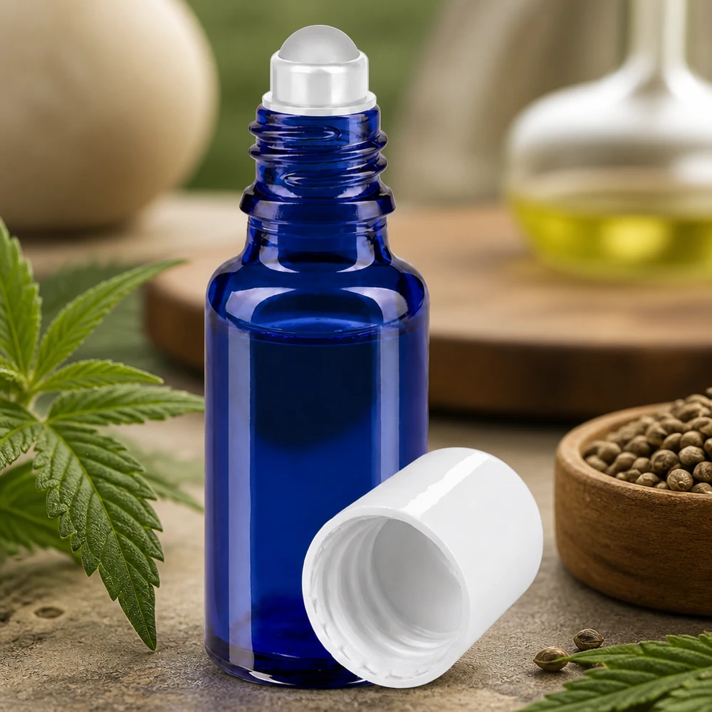 Blå 20 ml glasflaske med rullekugle og hvidt låg mellem hampeblade og frø