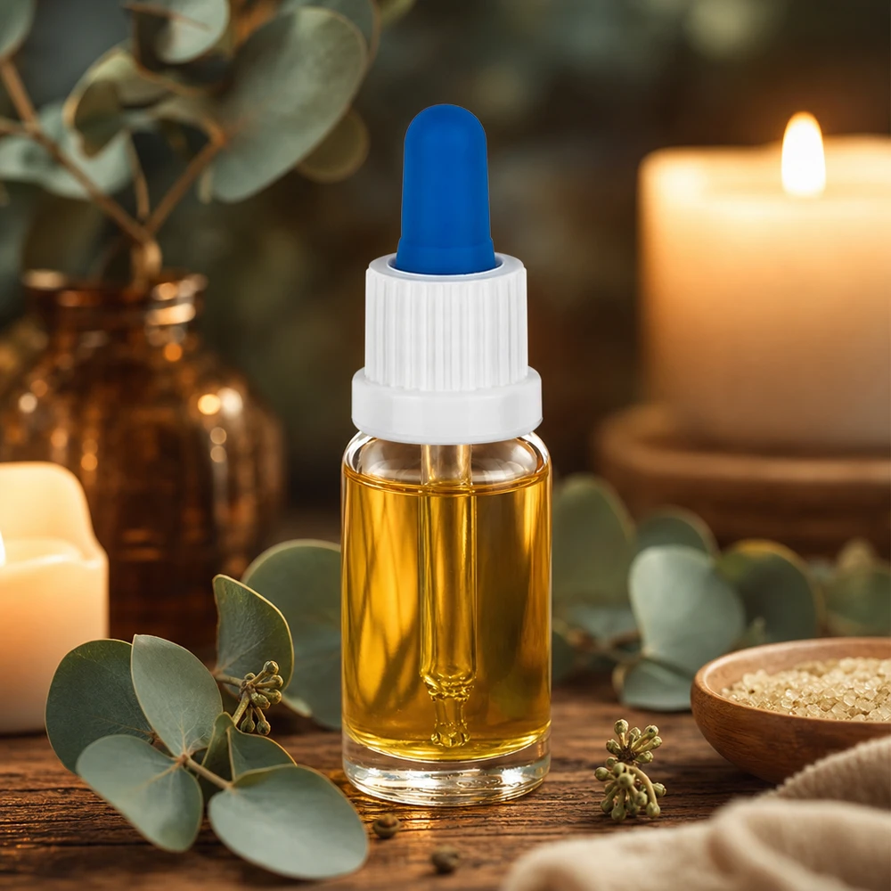 10 ml pipetteflaske hvid/blå OV ClearL. UT18/10 Lille 10 ml pipetteflaske med guldfarvet olie, hvid prop og blå gummikugle på et træbord
