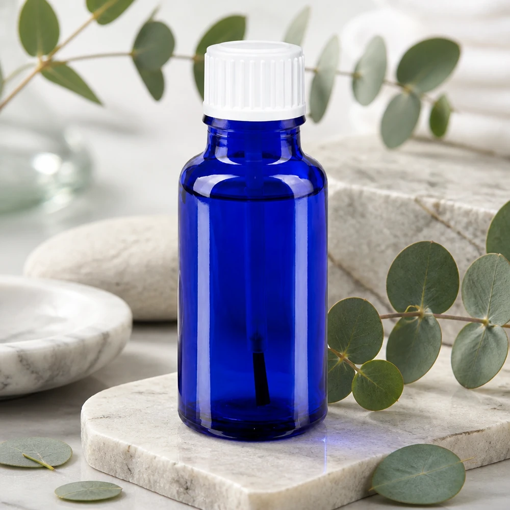 Koboltblå glasflaske på 20 ml med hvid pensel på marmor og eukalyptus