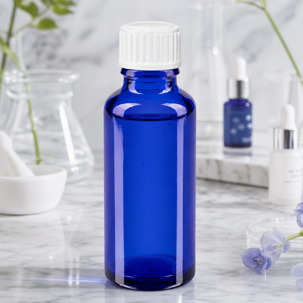 Cylindrisk 30 ml farmaceutisk glasflaske i koboltblå med hvid skruelåg på marmor