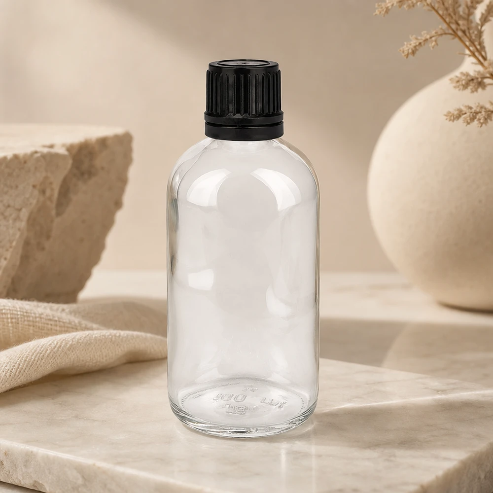 100ml (kugle)Flas. 8mm GR s. STD ClearL. UT18/100 Cylindrisk 100 ml flaske af klart glas med riflet sort låg på marmorunderlag