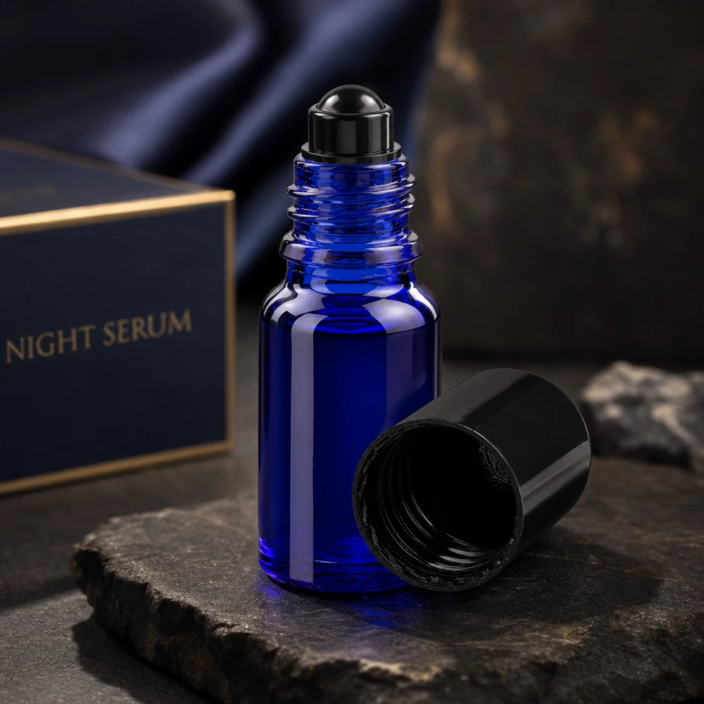Mørkeblå 10 ml ApoGlas-roll-on-flaske med åbent sort låg på en skifersten foran en Night Serum-æske