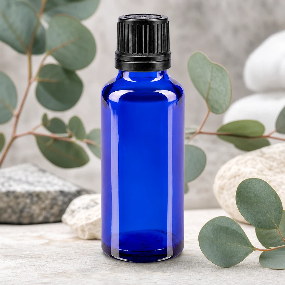 Apoteksflaske blå 30ml skruelåg sort hældeprop r. OV Lille blå glasflaske på 30 ml med sort originalitetslukning foran eukalyptusgrene