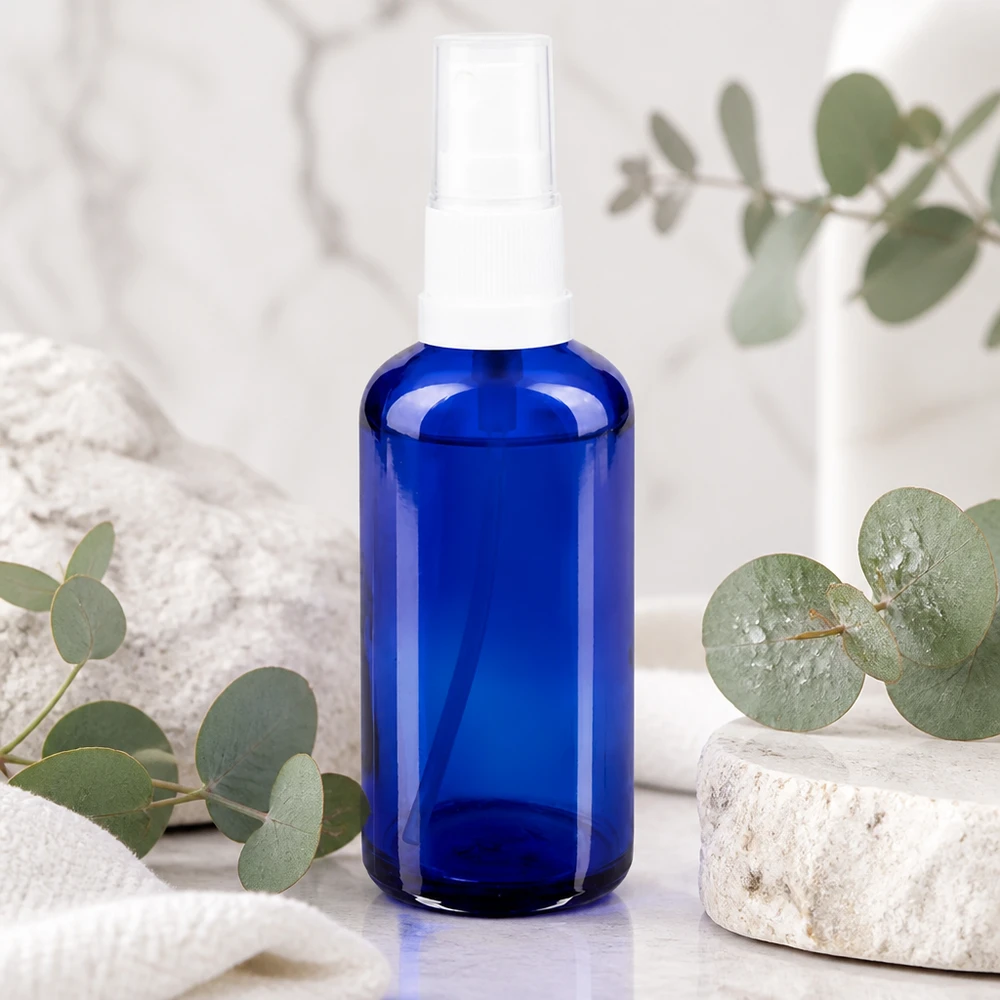 Apoteksflaske blå 50 ml spraytop hvid 50 ml blå glasflaske med hvid forstøver på marmor med eukalyptus