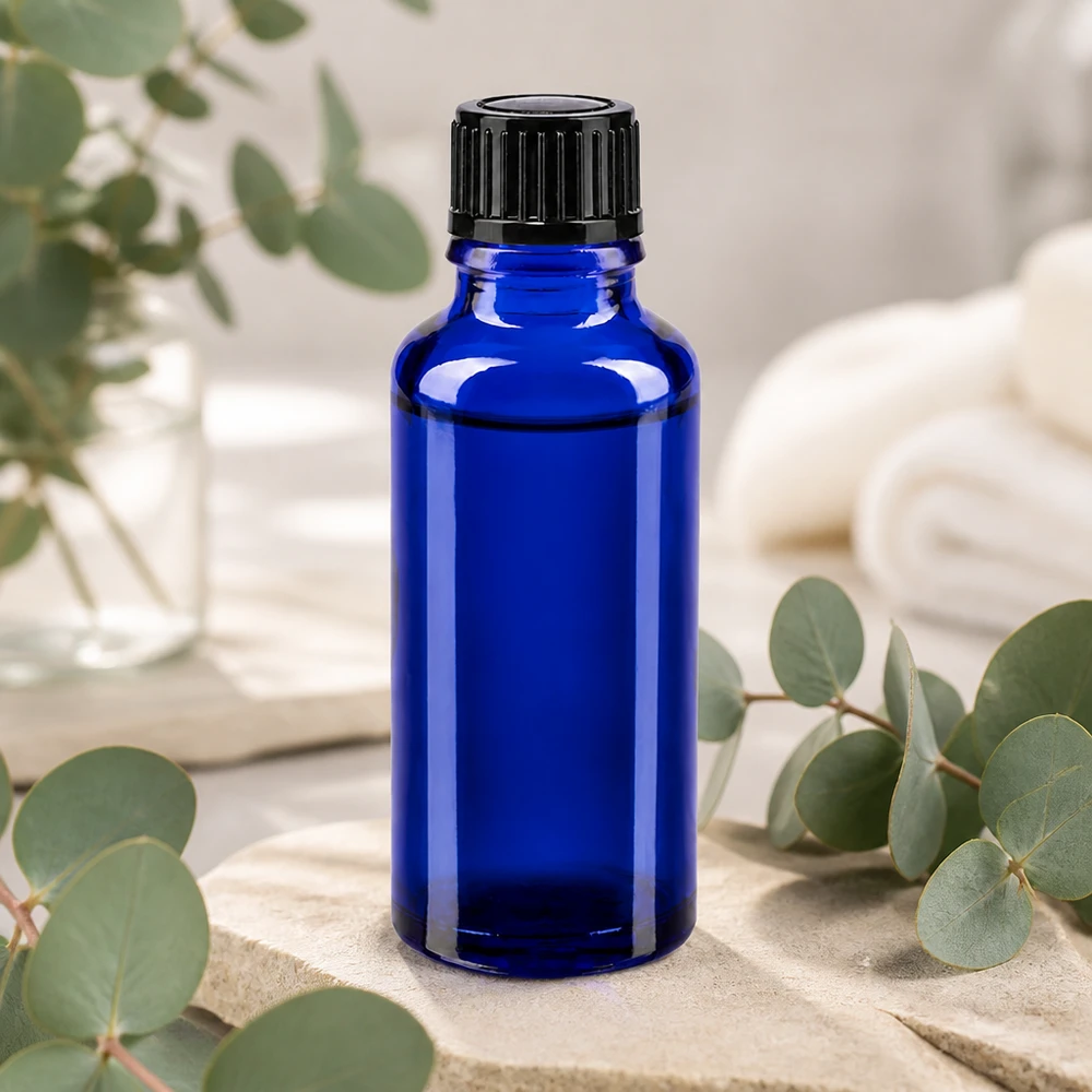 Koboltblå 30 ml glasflaske med sort doseringshætte på natursten med eukalyptusgrene