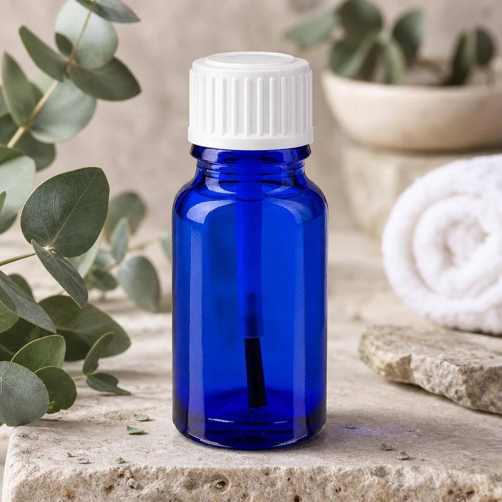 Blå 10 ml glasflaske med hvid penselkappe ved siden af eukalyptusgrene på natursten