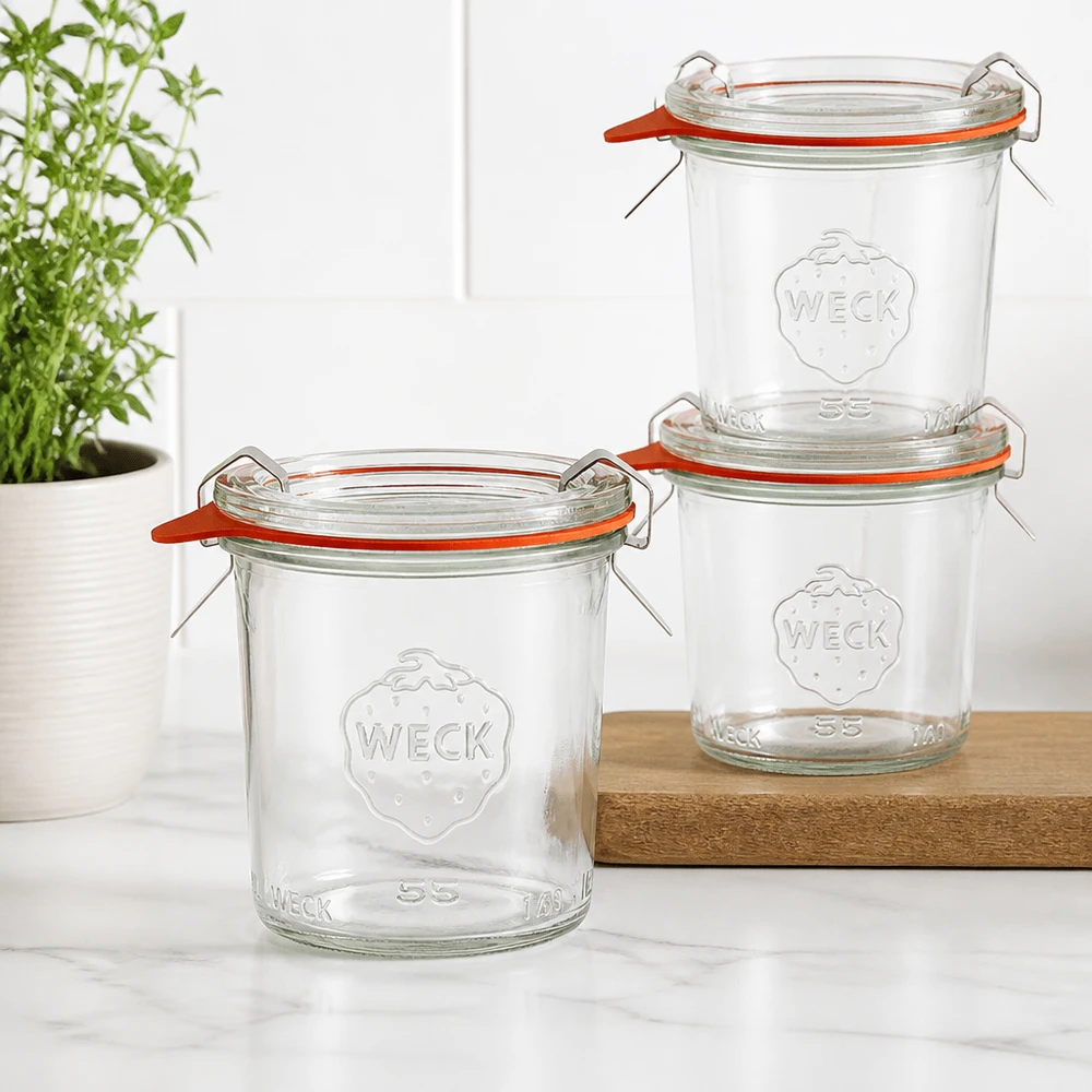 140 ml Briller komplet WECK RR60 Tre WECK 140 ml RR60-tumblere stablet på en træplade i et moderne køkken med en grøn plante i baggrunden.