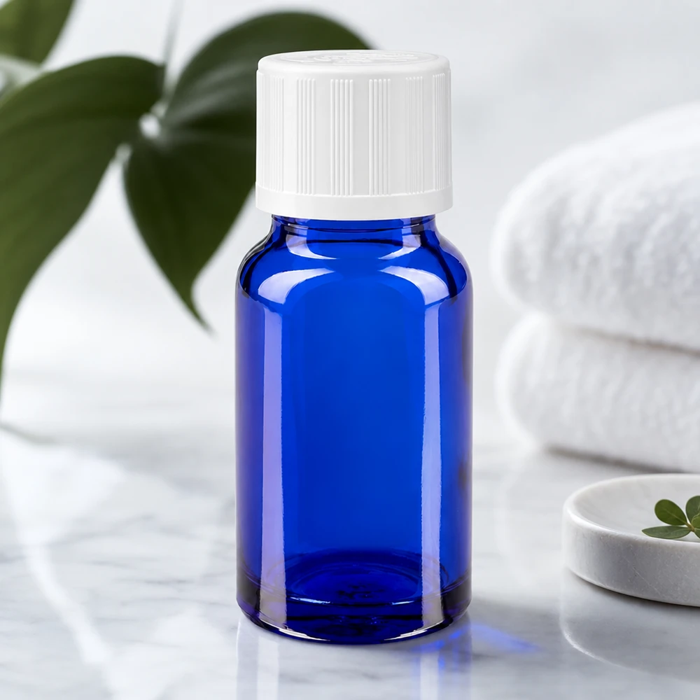 Apoteksflaske blå 10ml dråbetæller hvid KiSi St 10 ml blåt apotekerglas med hvidt børnesikret låg på marmor ved siden af sammenfoldede håndklæder