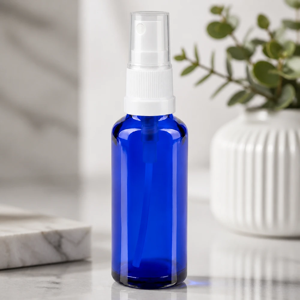 Apoteksflaske blå 30 ml spraytop hvid Blå 30 ml apotekerflaske af glas med hvidt sprøjtehoved på en hvid marmorbaggrund
