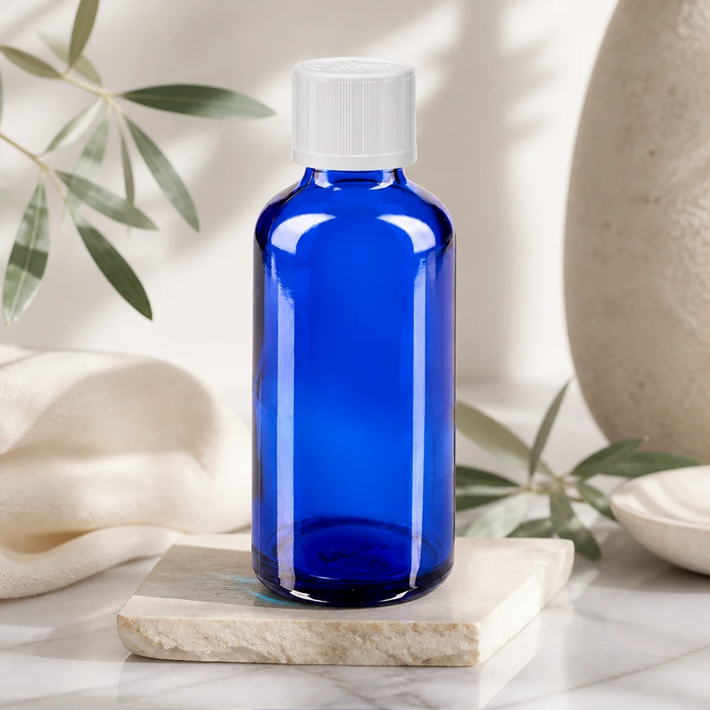 Apoteksflaske blå 50ml dråbetæller hvid KiSi St Blå glasflaske på 50 ml med hvid skruelåg på en marmorsten i et lyst, naturligt miljø